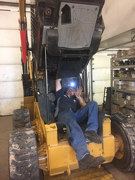 A man is sitting on the back of a bulldozer in a garage.