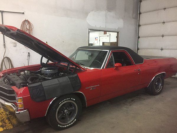 A red car with the hood up is parked in a garage.