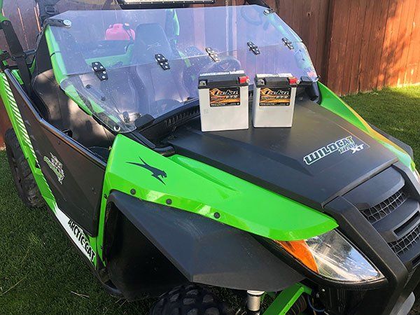 A green and black atv with two batteries on the hood.
