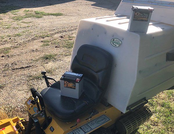 A yellow and white lawn mower with a battery on the seat