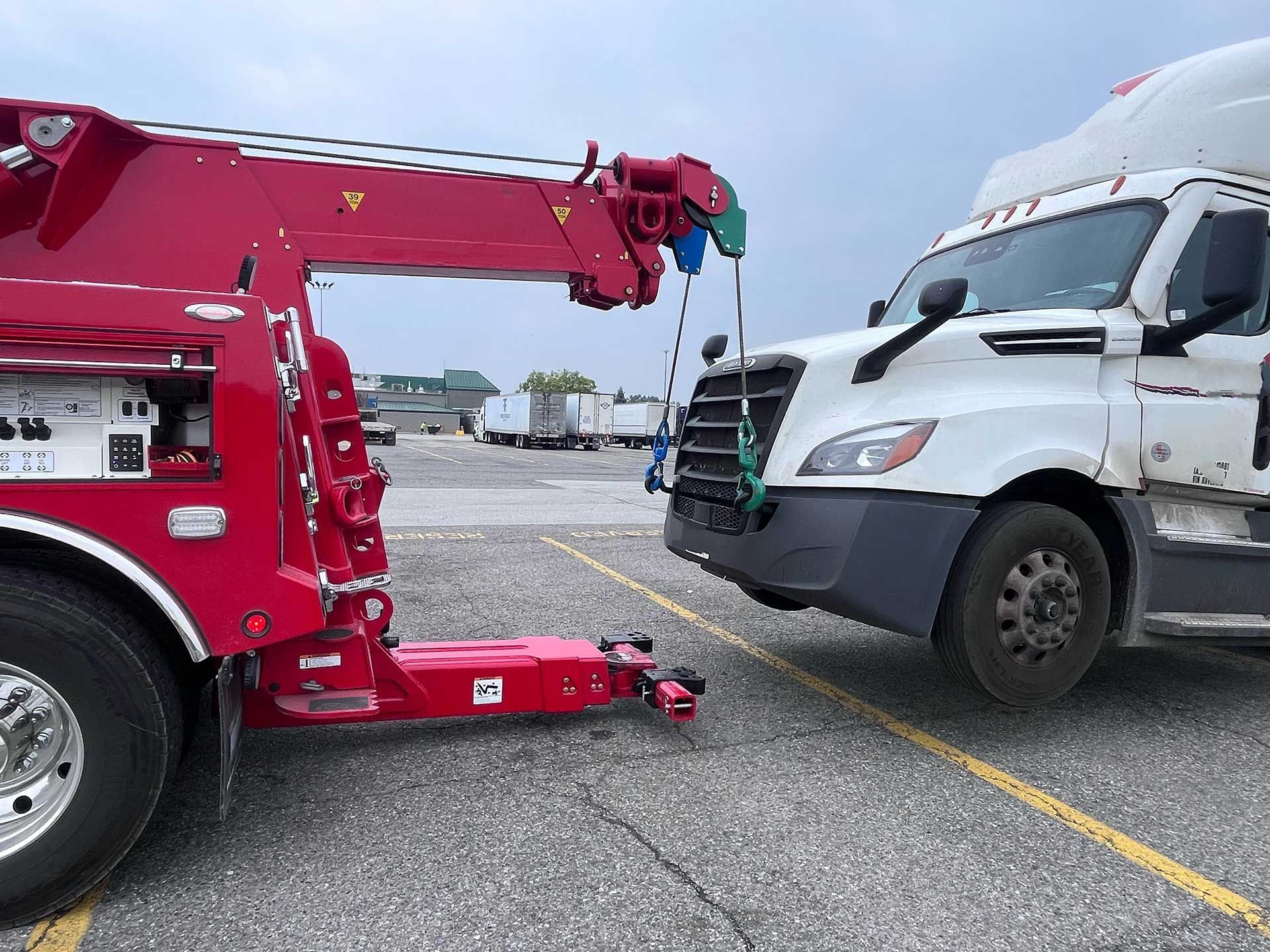 Red tow truck lifting the front of a white van in a parking lot