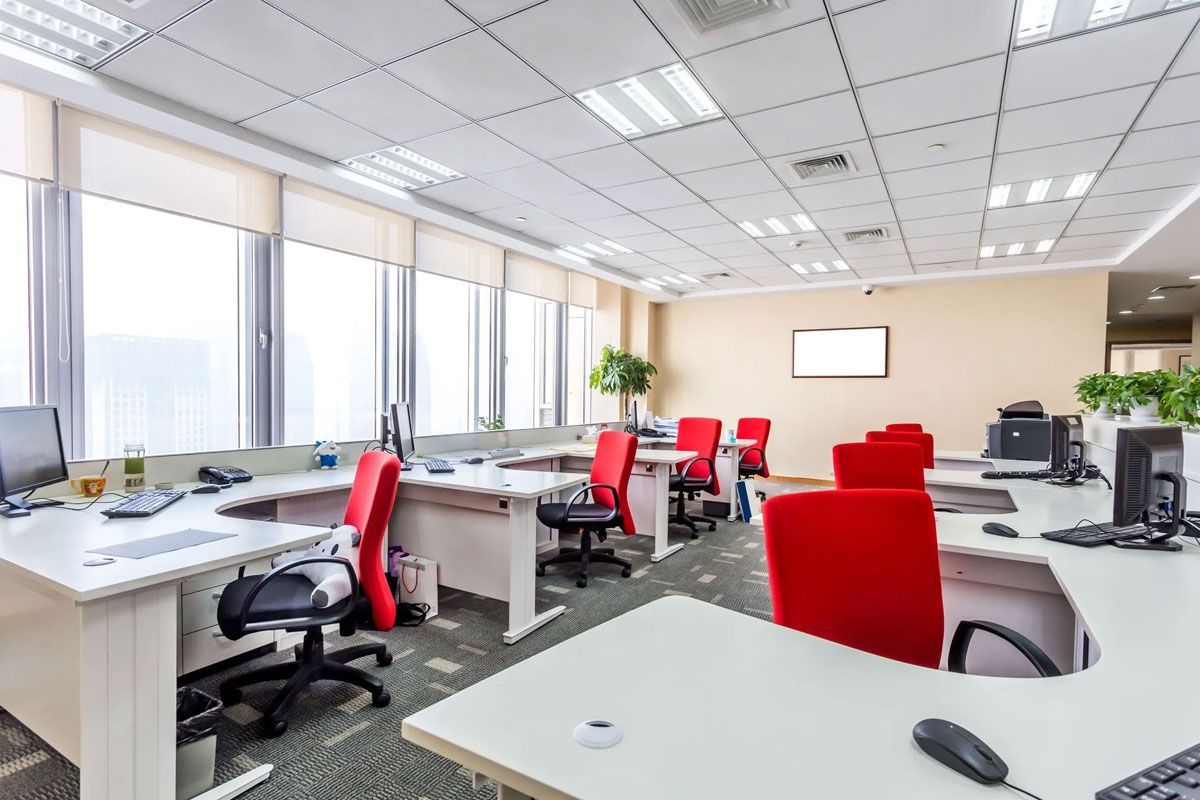 Modern open-plan office with red chairs, desks, computers, and large windows