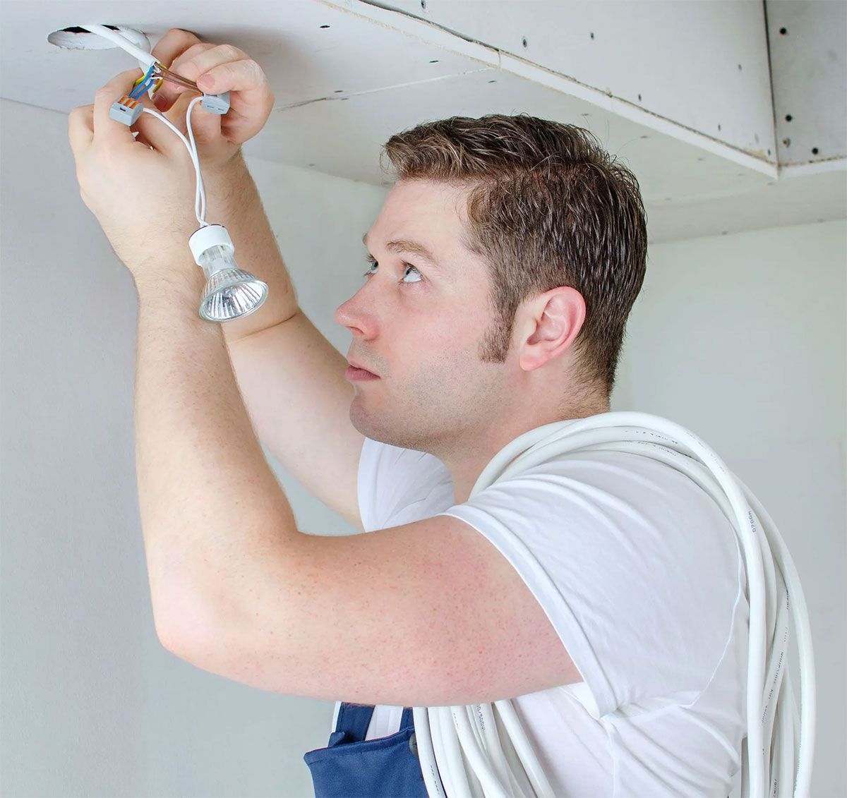 Electrician installing a ceiling light fixture with tools in a white room