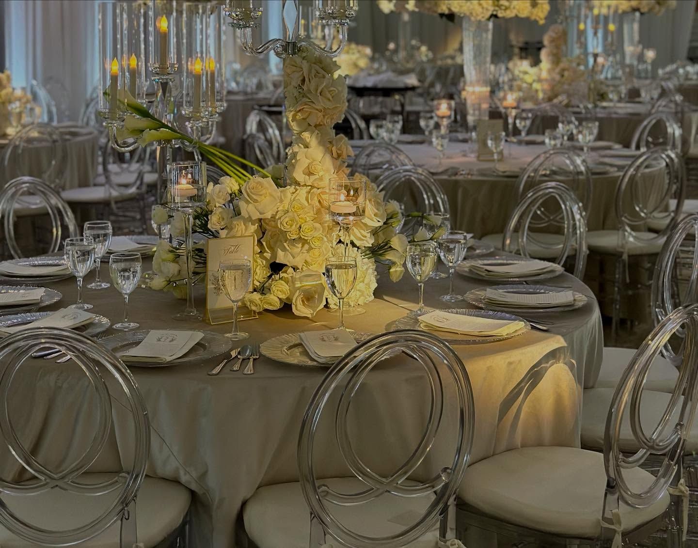 Elegant wedding reception with round tables, clear chairs, and floral centerpieces.