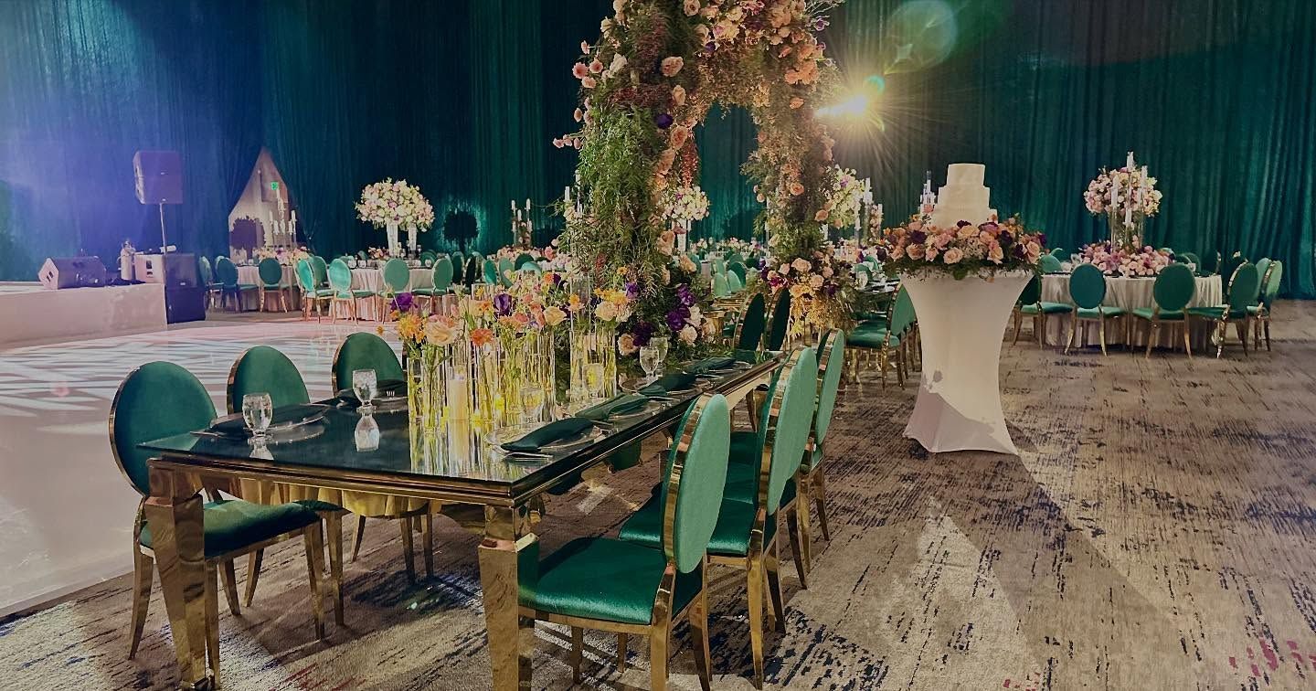 Elegant wedding reception with emerald chairs, tables, arch, flowers, and a cake.