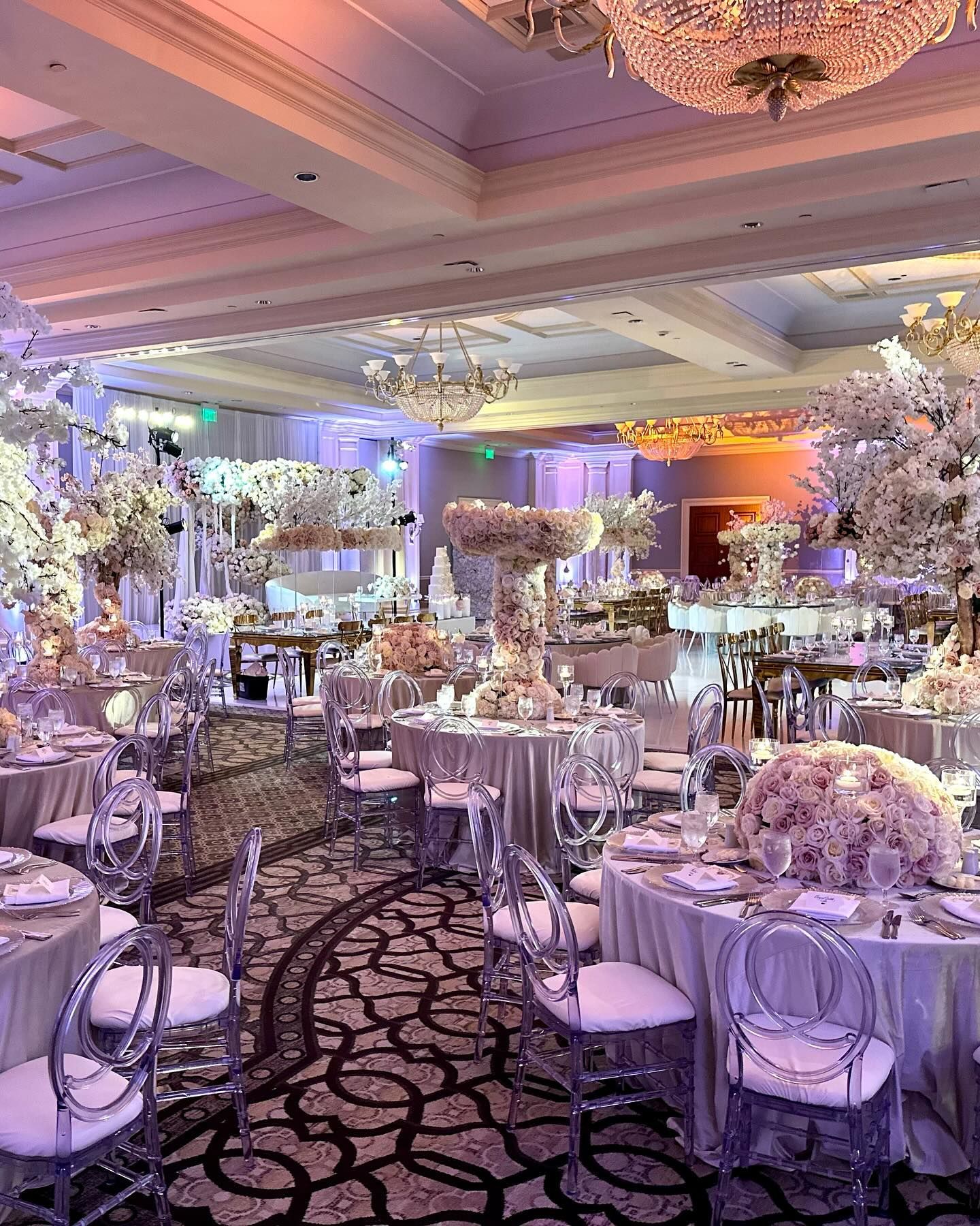 Elegant ballroom decorated for a wedding with round tables, floral arrangements, and crystal chandeliers.