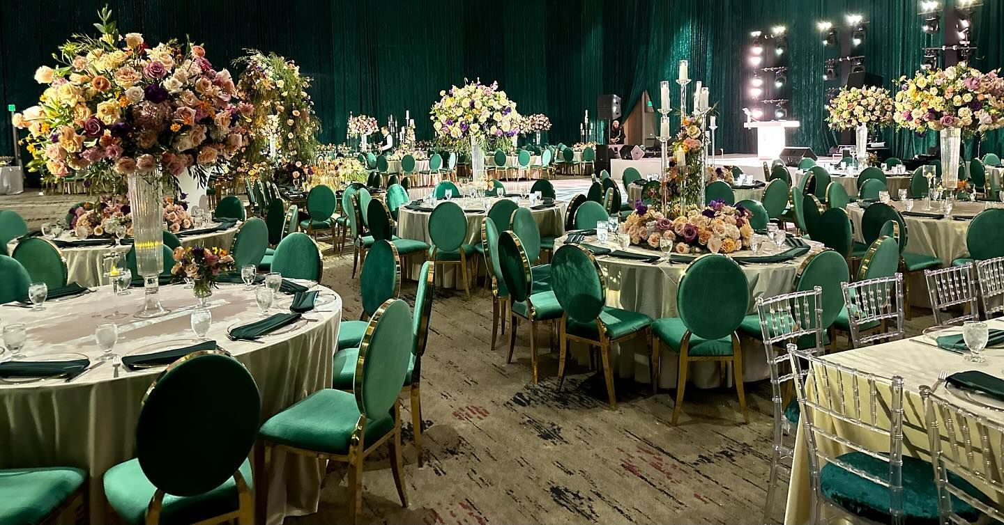 Emerald green banquet hall with round tables, floral centerpieces, and green chairs.