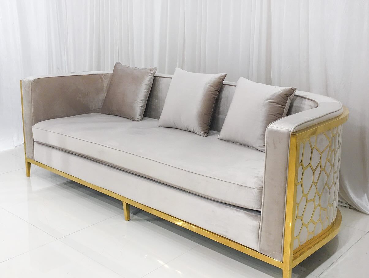 Beige velvet sofa with gold trim and pillows, against a white backdrop.