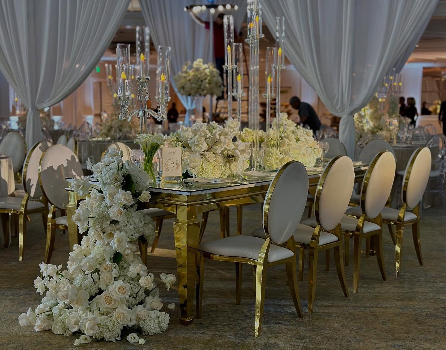 Elegant wedding reception table with white floral arrangements and gold chairs.