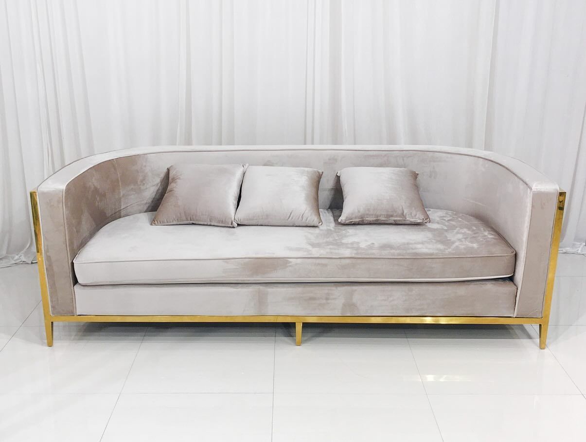 Beige velvet sofa with gold frame and three matching pillows.