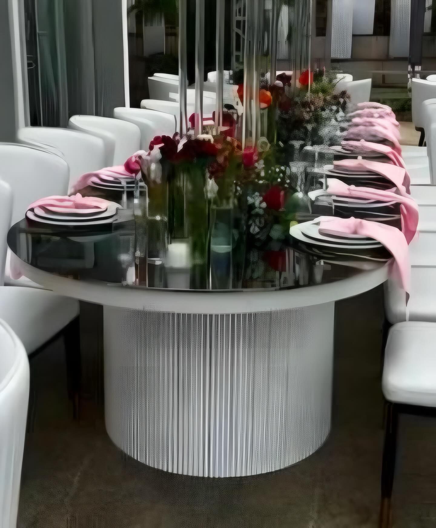 Elegant round table set for dining with floral centerpiece and pink napkins.