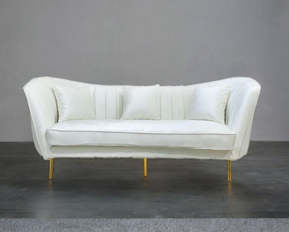 White velvet sofa with gold legs and two white pillows against a gray backdrop.