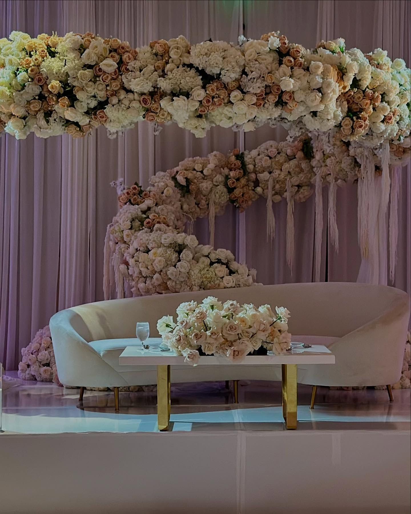 White couch with floral archway backdrop, stage setting.