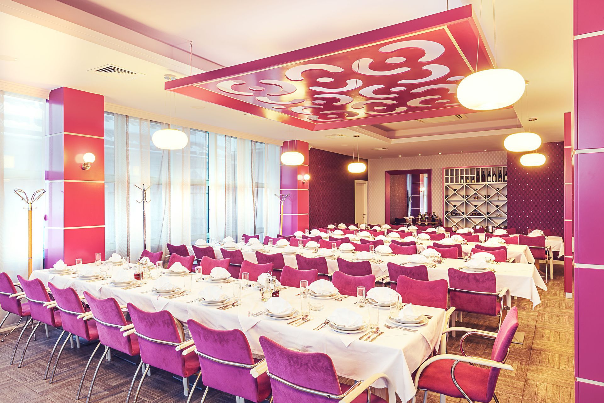 A formal dining room with pink accents; long tables set for a banquet, rows of pink chairs.