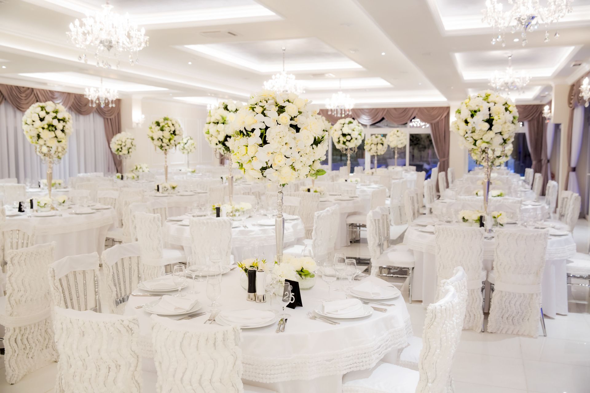 Elegant white wedding reception tables with floral centerpieces and chandeliers.