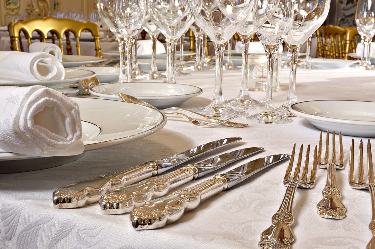 Formal dining table set with silverware, glassware, white plates, and rolled napkins.