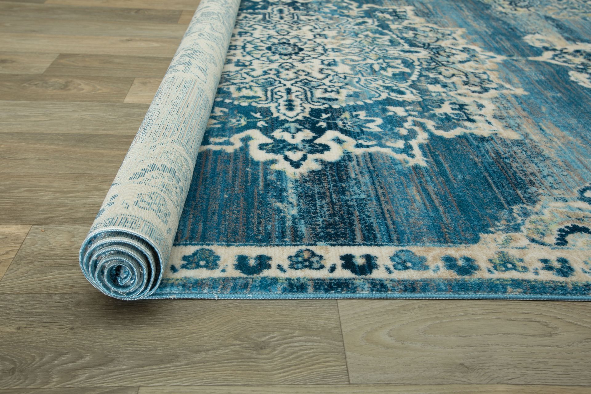Rolled-up blue and white patterned rug on light-colored wood flooring.
