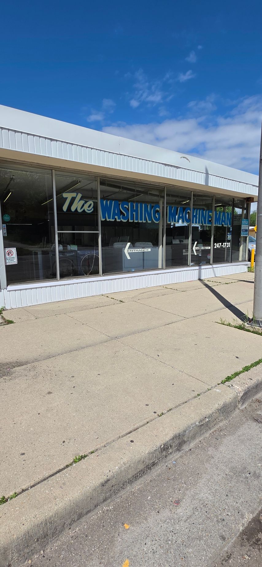 Storefront with large windows and blue signage along a sidewalk under a clear blue sky
