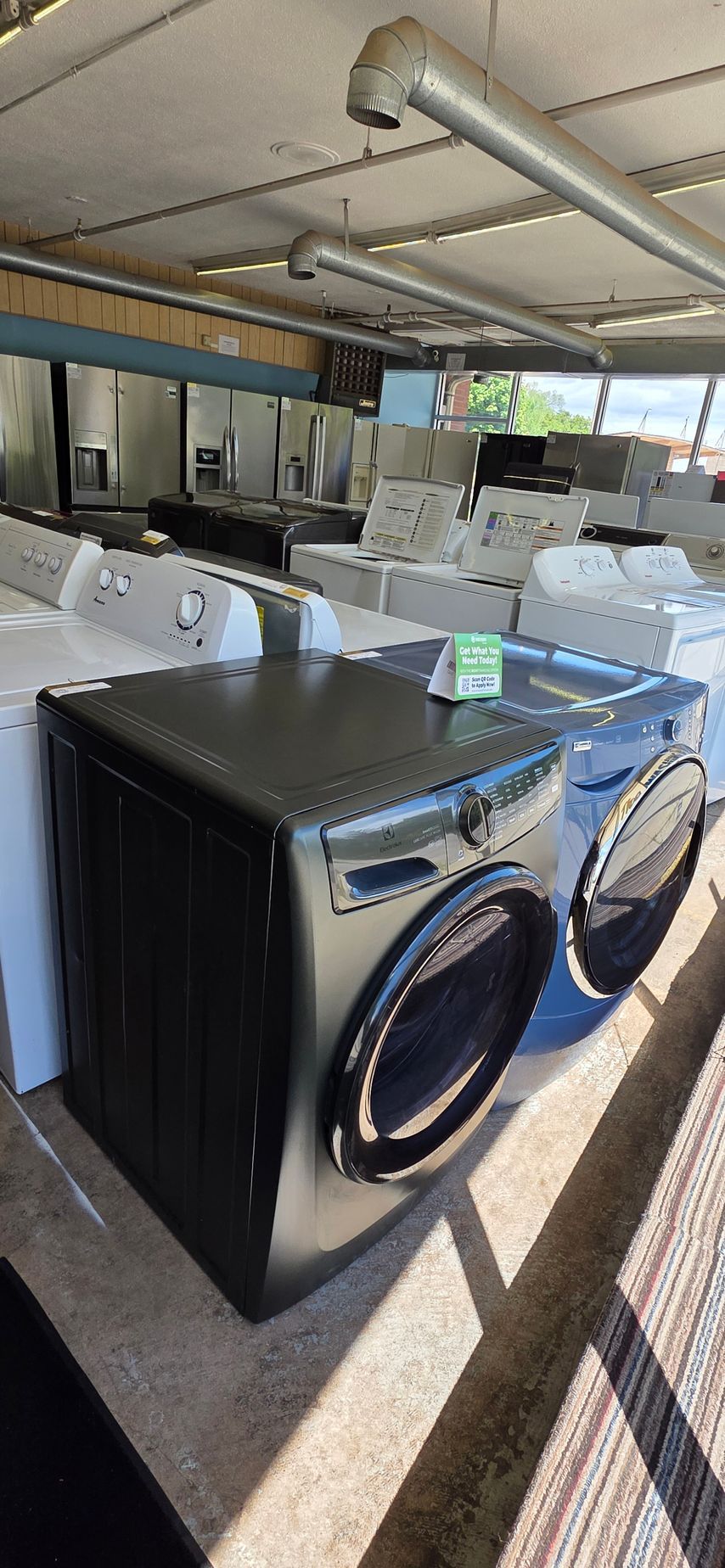 Black front-load washer and dryer in a laundromat, with sunlight casting shadows across the floor.