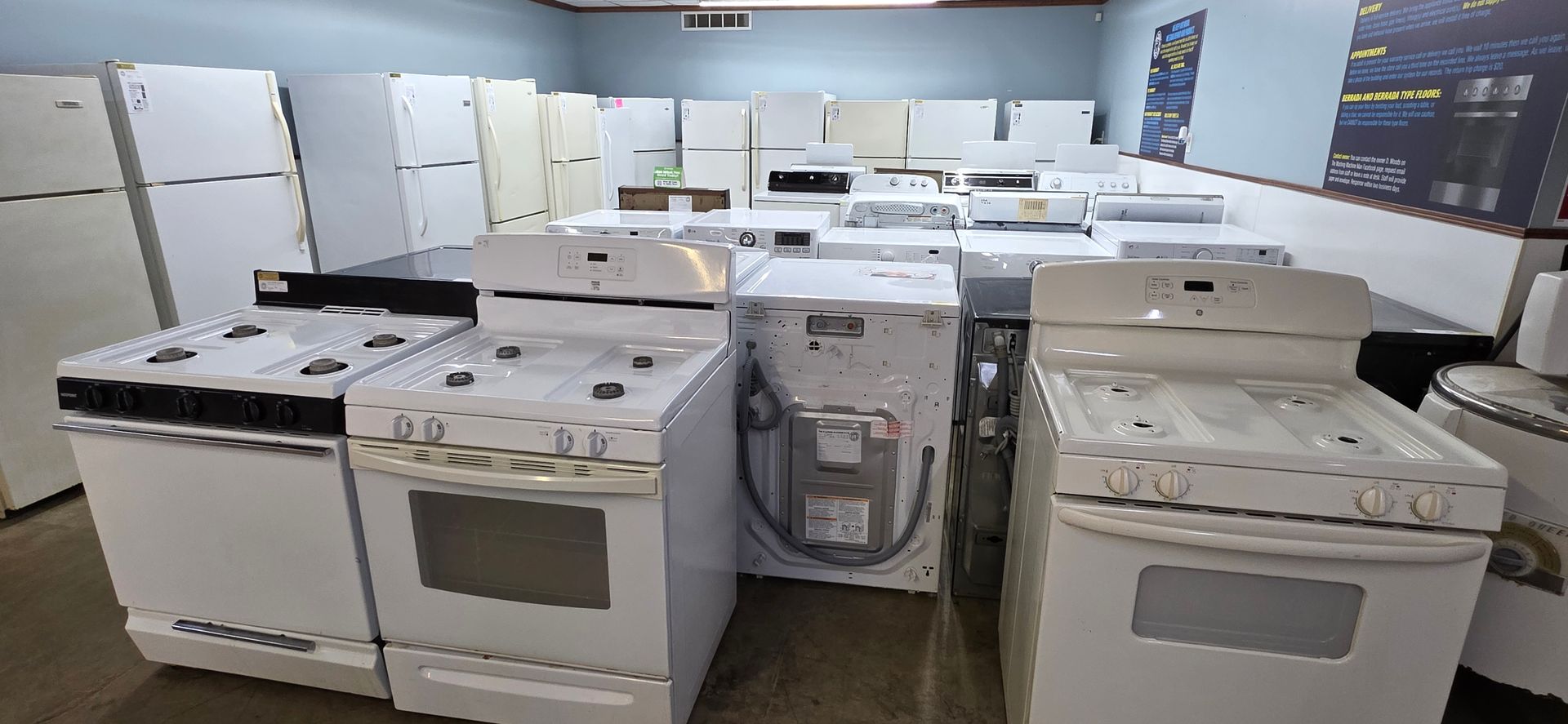 Appliance showroom with rows of white stoves and ovens displayed indoors