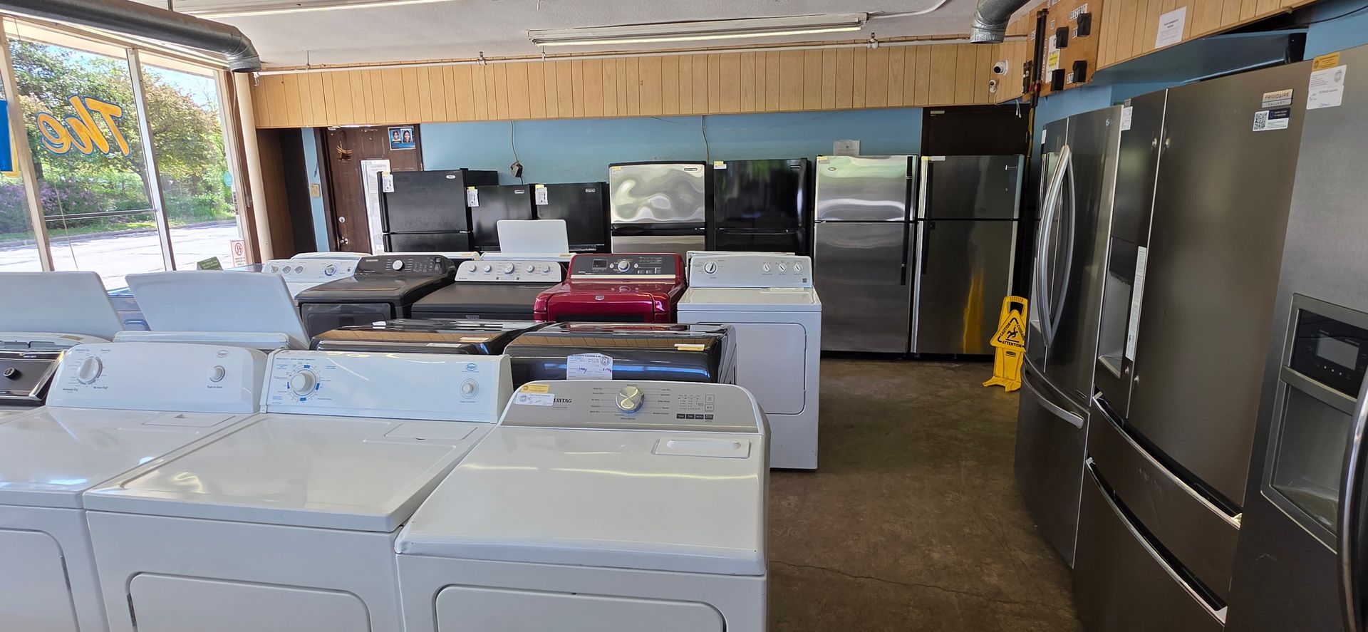 Warehouse-style appliance showroom with rows of white washers and stainless steel refrigerators
