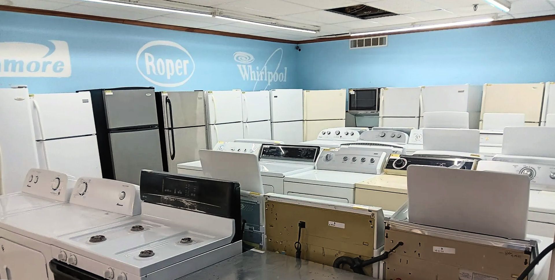 Laundry appliance showroom with rows of washers and dryers under blue brand signage