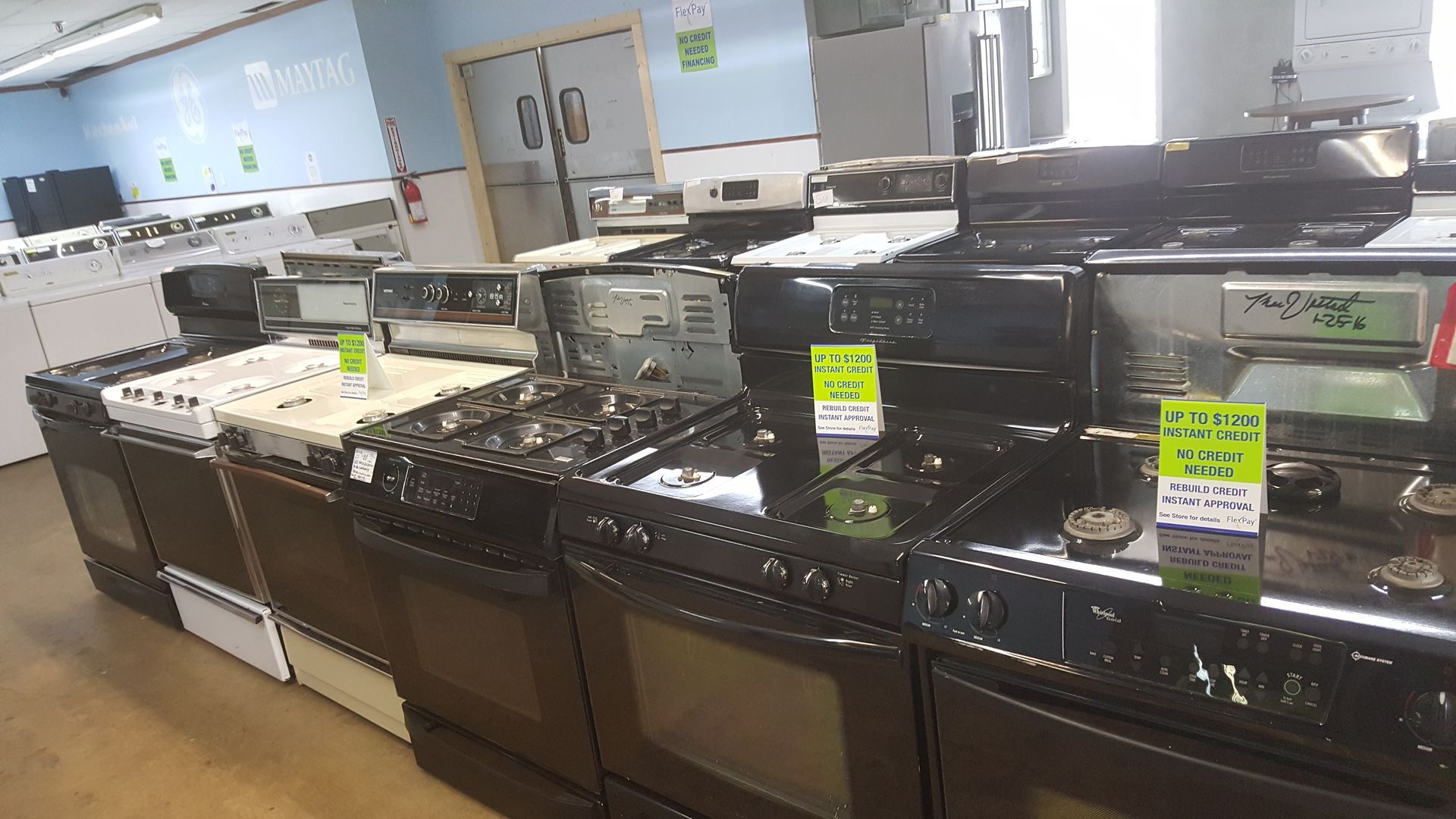 Row of used black and white kitchen stoves on display in a store showroom