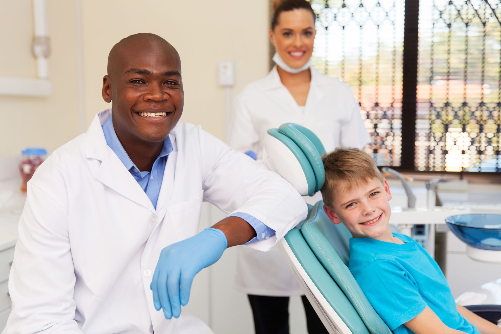 Dentist and assistant smiling with a child in a dental chair, bright clinic setting