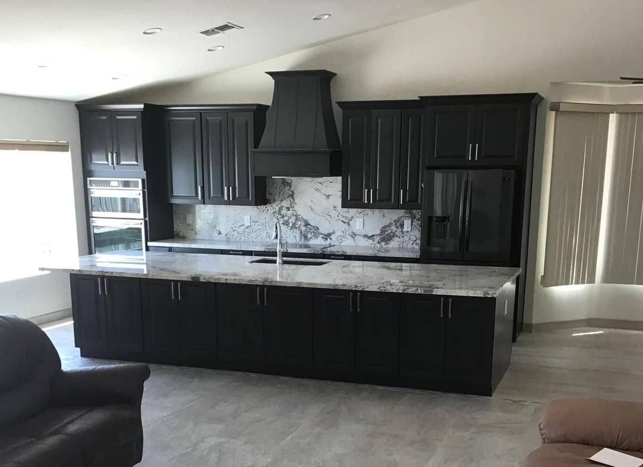 a kitchen with black cabinets and granite countertops in a living room