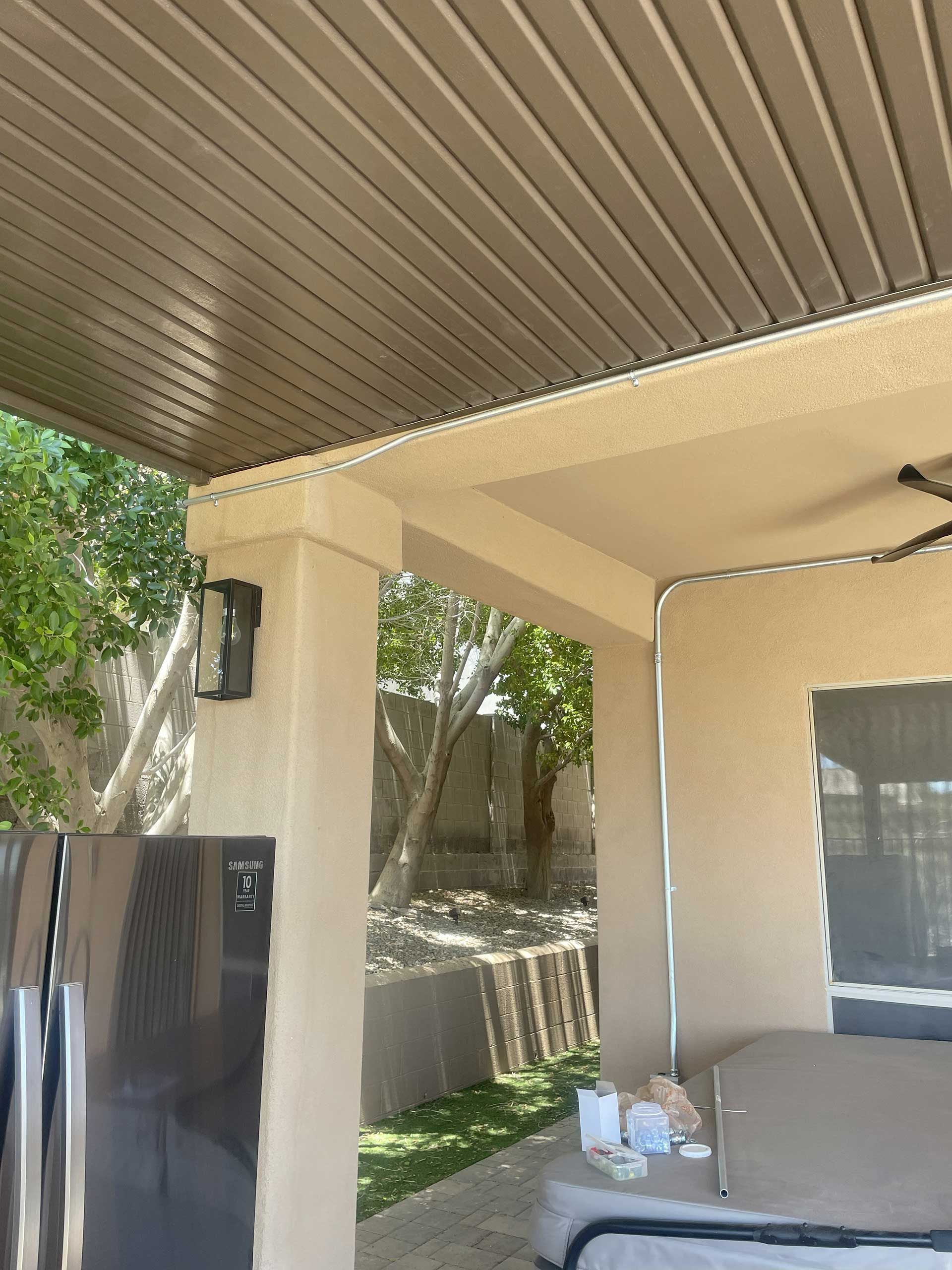 a patio with a brown ceiling, beige pillars, a refrigerator, and a view of greenery