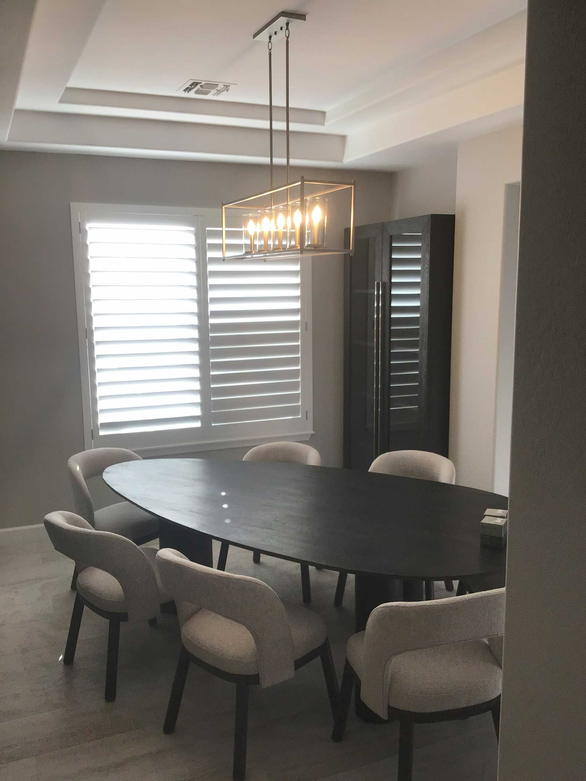dining room with an oval dark wood table, six curved-back chairs, a rectangular chandelier, and window with shutters
