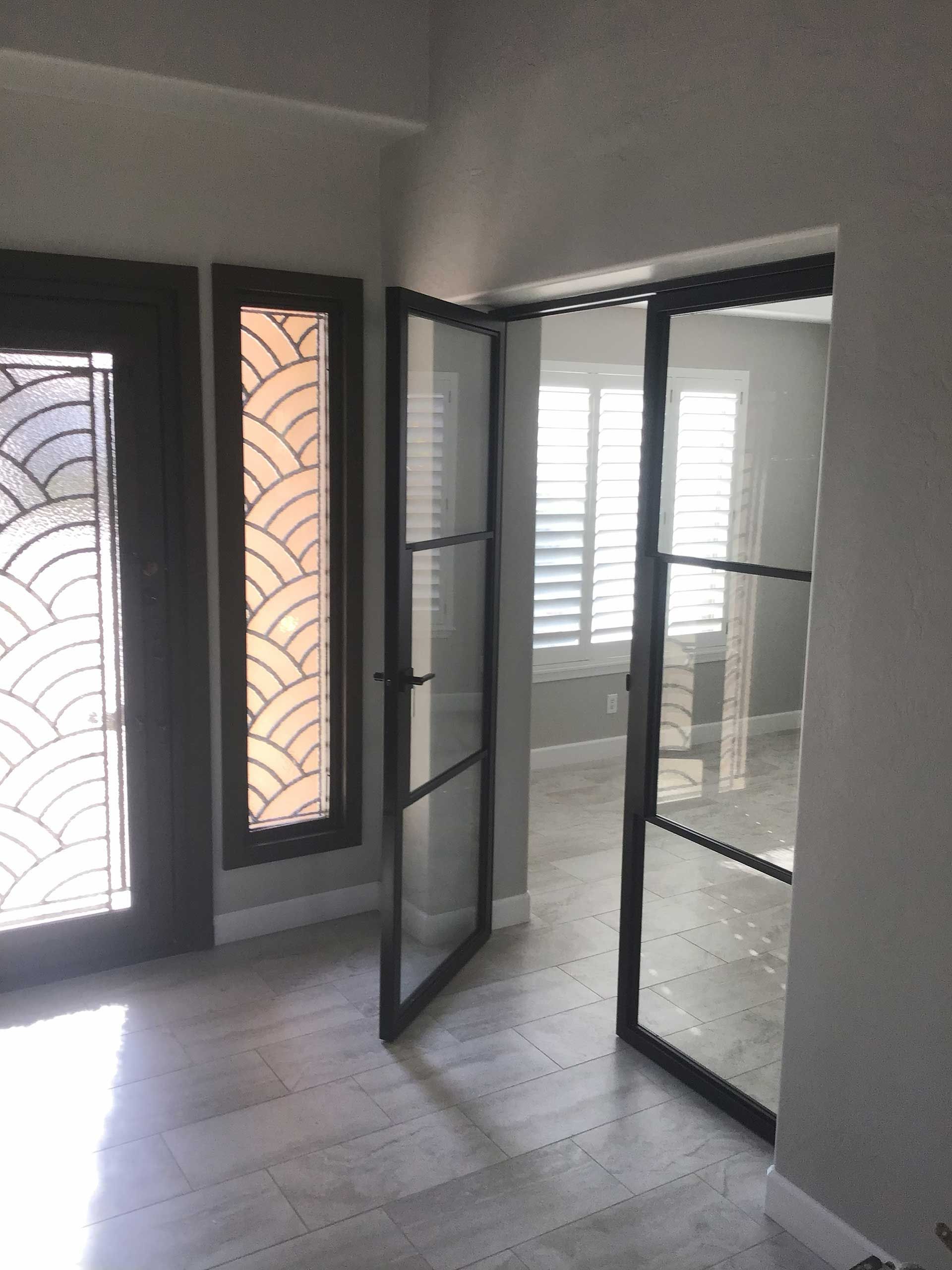 entryway with open glass doors, featuring a decorative window and door with geometric patterns on the left and a room with shutters in the background
