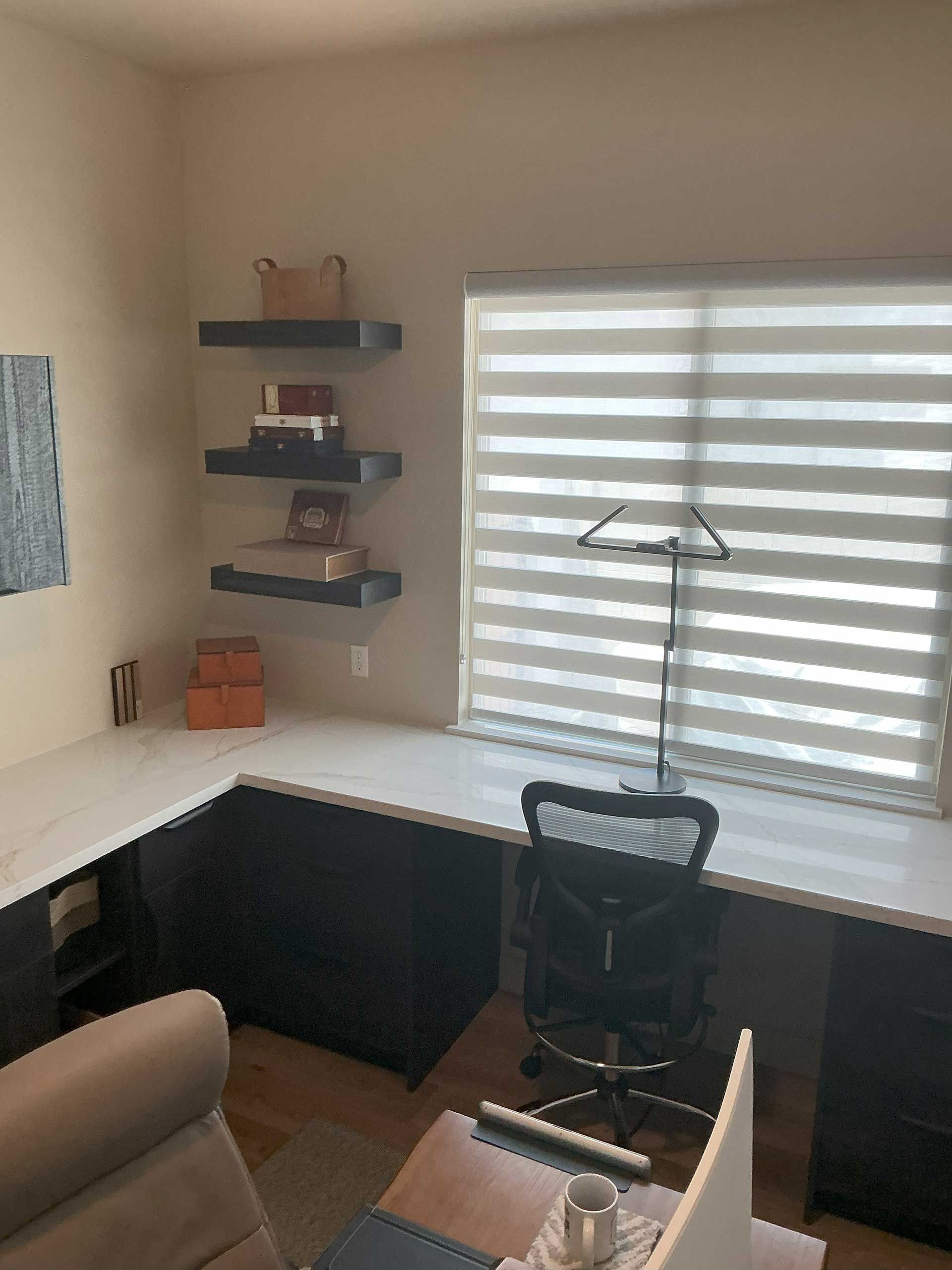 corner home office with dark cabinetry and white countertops, a desk chair, and a window with blinds
