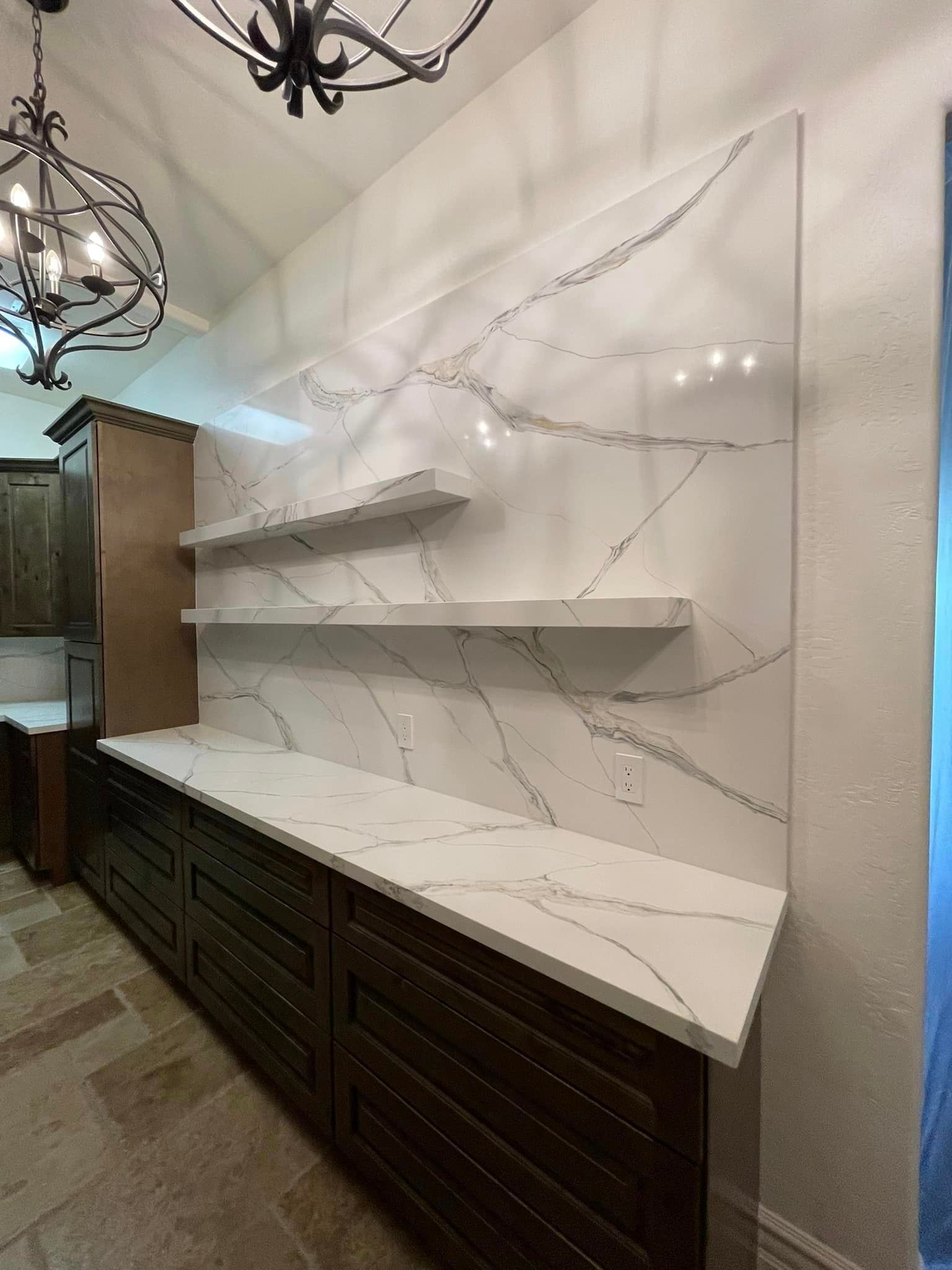 A kitchen with a marble counter top , wooden cabinets , and a chandelier.