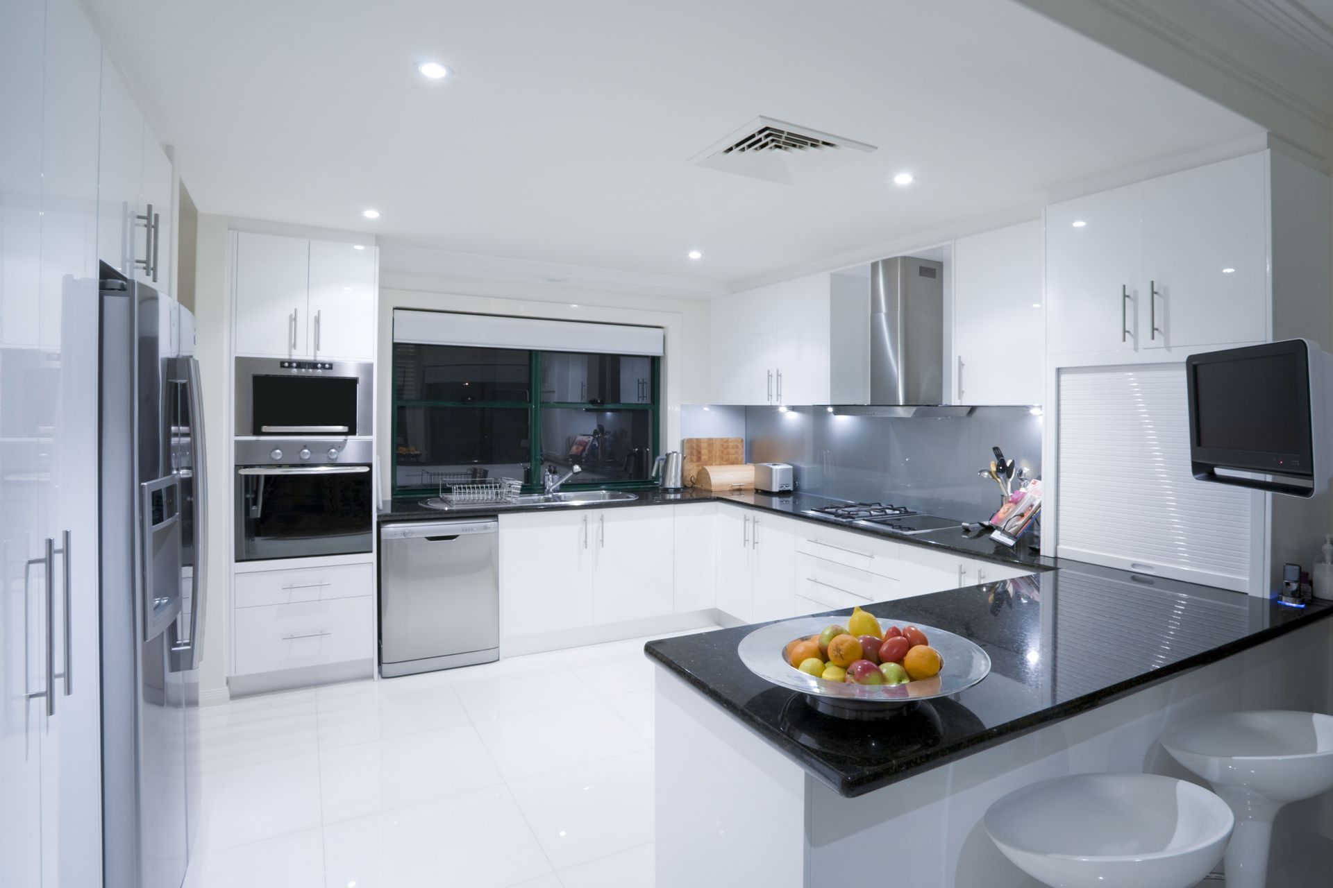 A kitchen with white cabinets and black counter tops and a bowl of fruit on the counter.