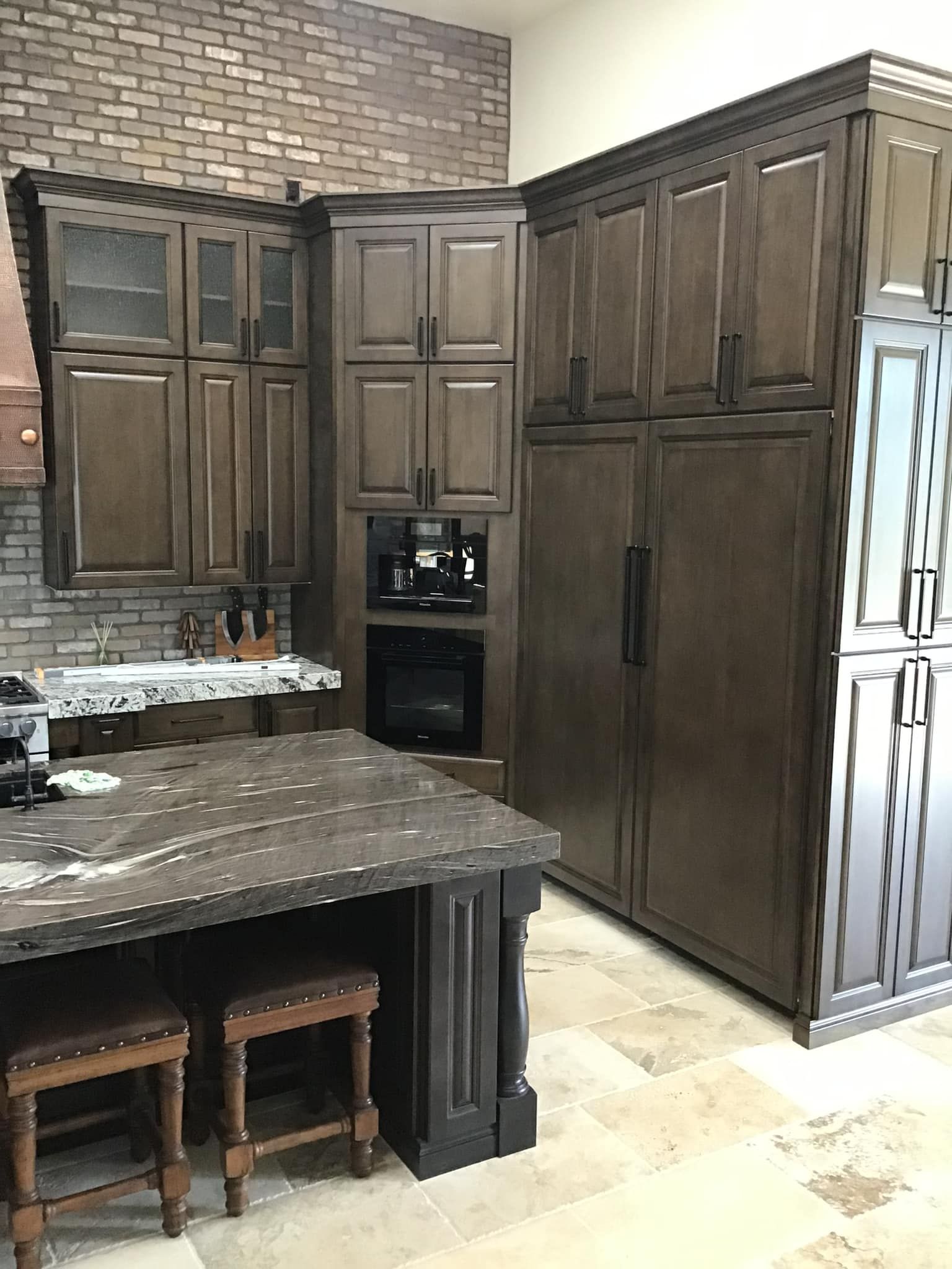 A kitchen with wooden cabinets and stools and a brick wall.