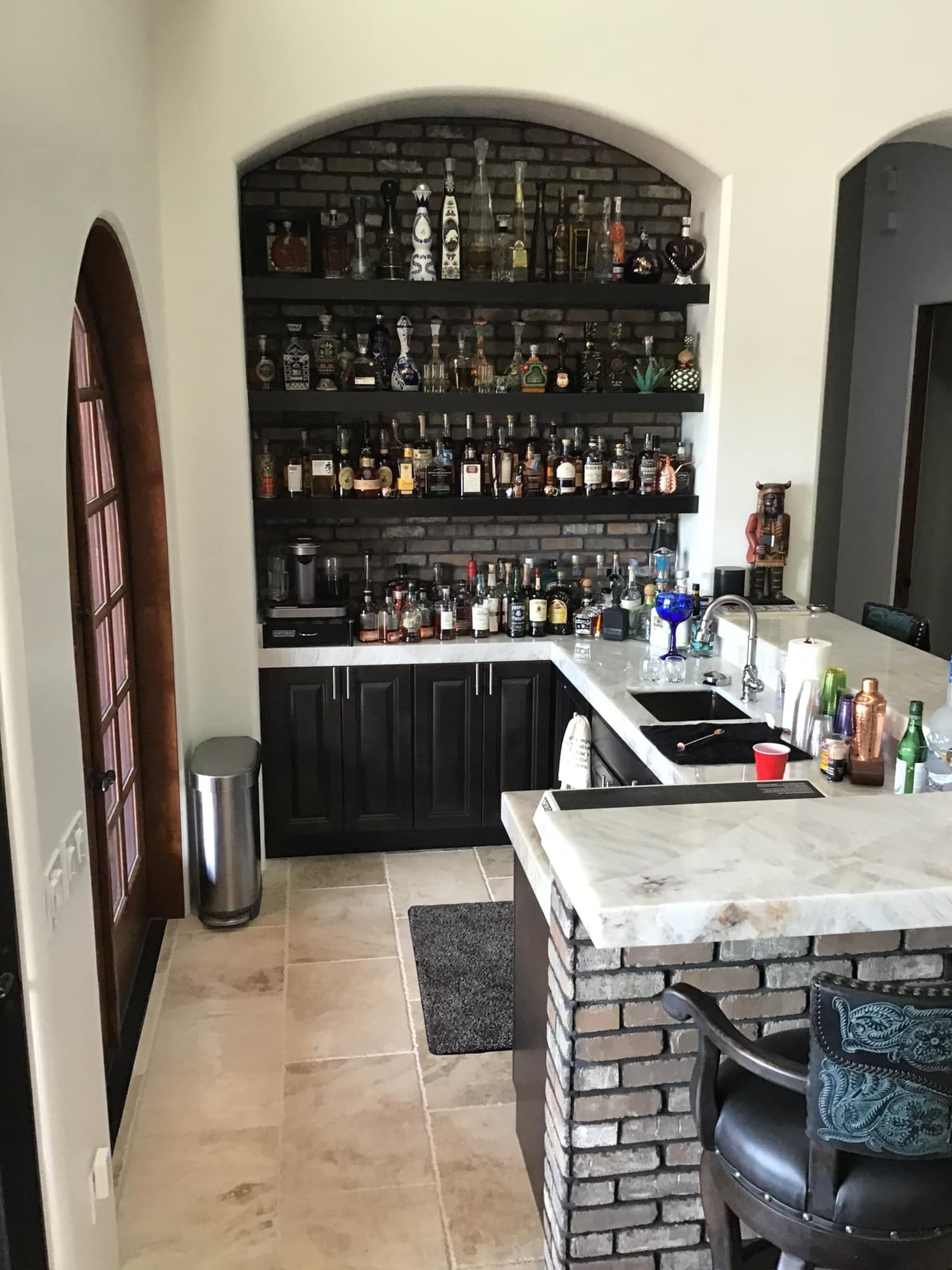 A kitchen with a bar and shelves filled with bottles of liquor.
