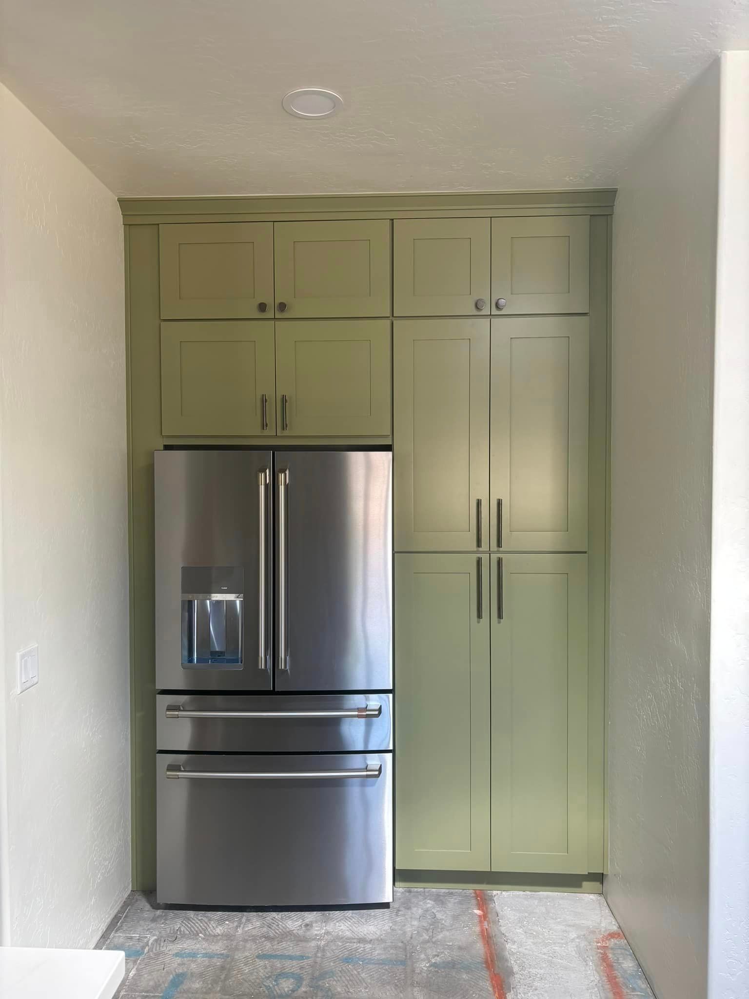A kitchen with green cabinets and a stainless steel refrigerator.