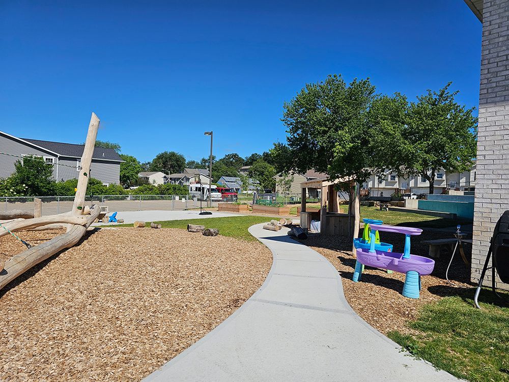 A walkway leading to a playground with a brick building in the background.