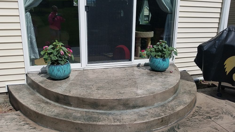A concrete porch with steps and potted plants in front of a house.