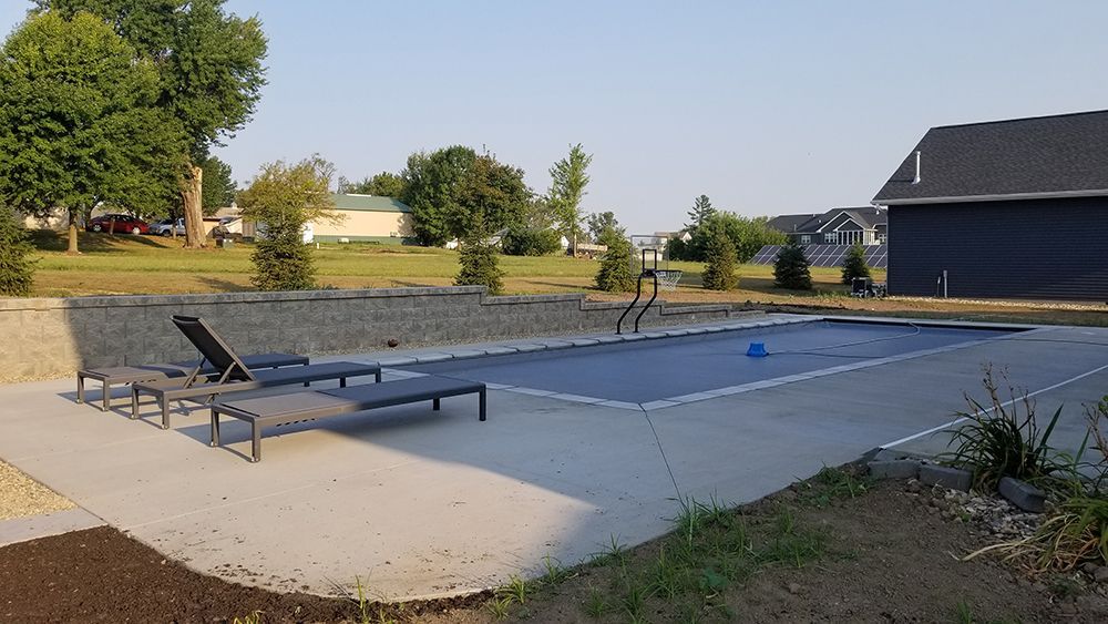 A large swimming pool is surrounded by lawn chairs and a house.