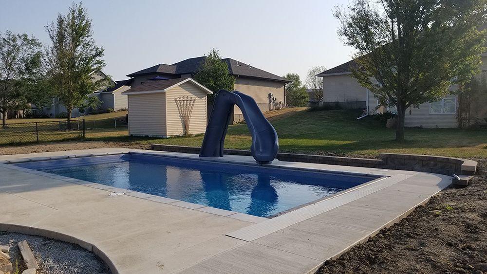 A swimming pool with a slide in the backyard of a house.