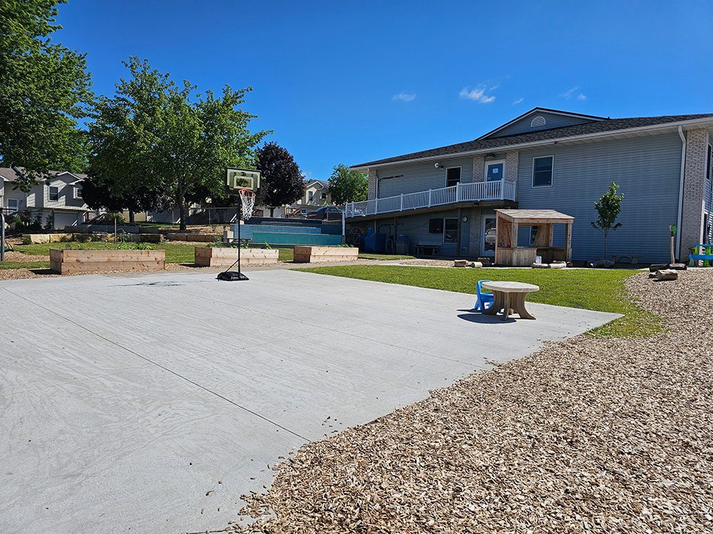 A basketball hoop is in the middle of a concrete court in front of a building.