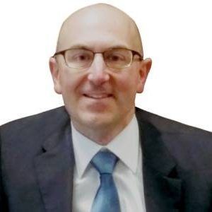 Man with glasses and a blue tie, smiling, wearing a suit.