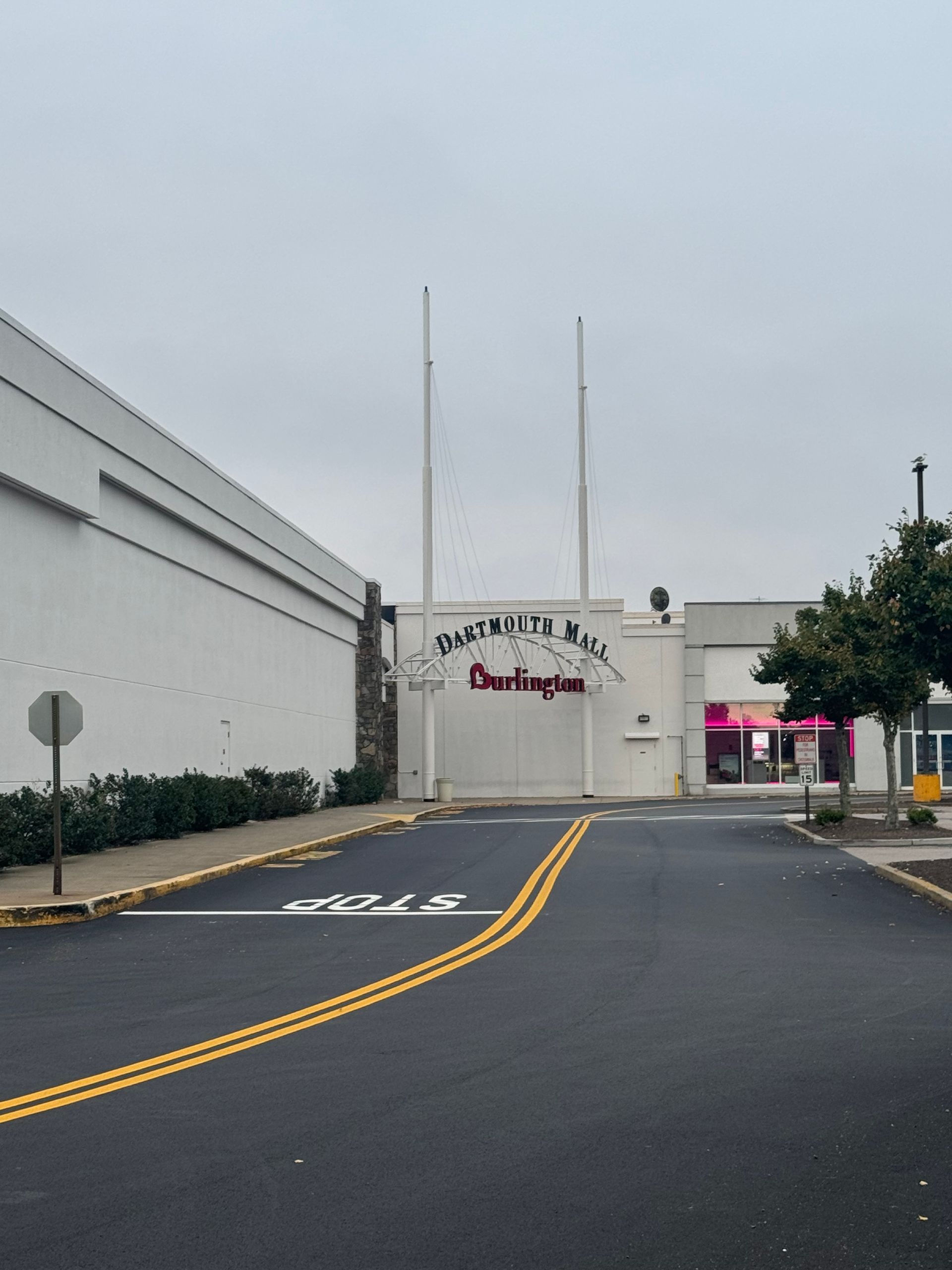 Driveway leading to a white building with signage, yellow lane markings, and an overcast sky.