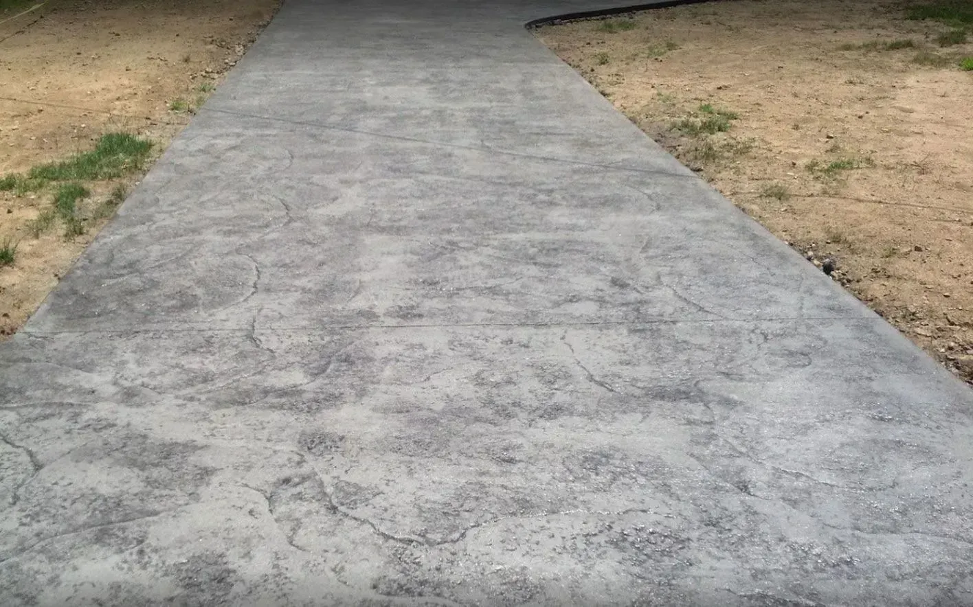 A long, textured gray concrete walkway curves through bare dirt and patchy grass.