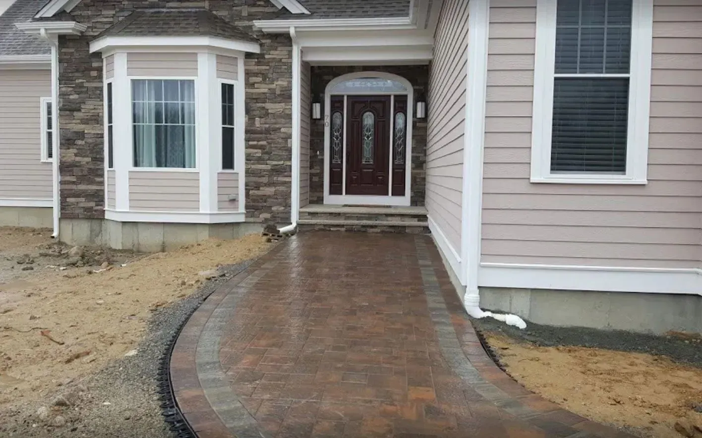 A stone walkway leads to the front entrance of a light pink house with stone accents and a white-trimmed door.