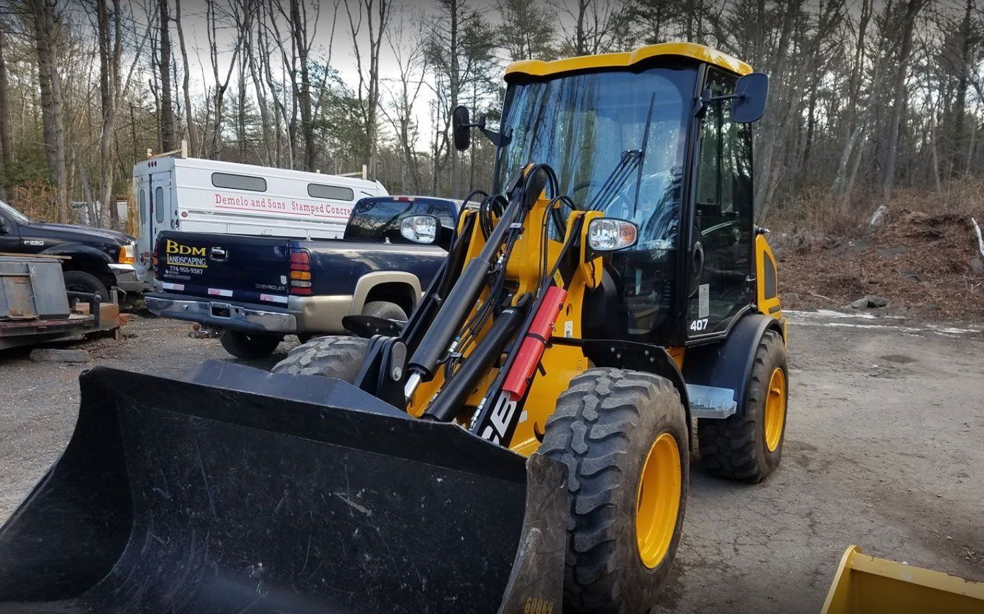 A yellow front-end loader parked on a dirt lot with a pickup truck in the background.