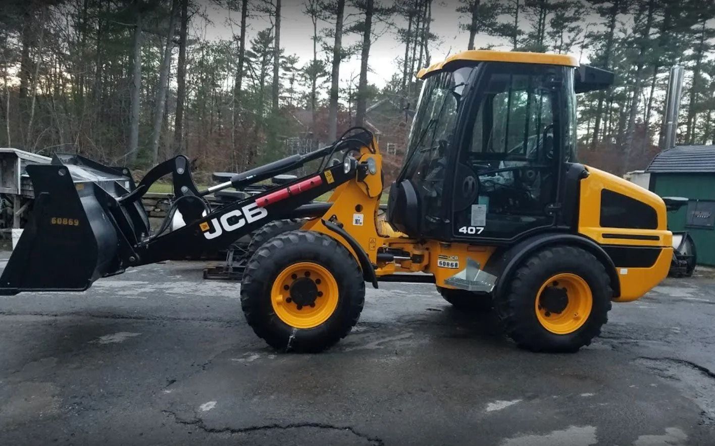 A yellow JCB 417 wheel loader with a black bucket parked on an asphalt surface in a wooded area.