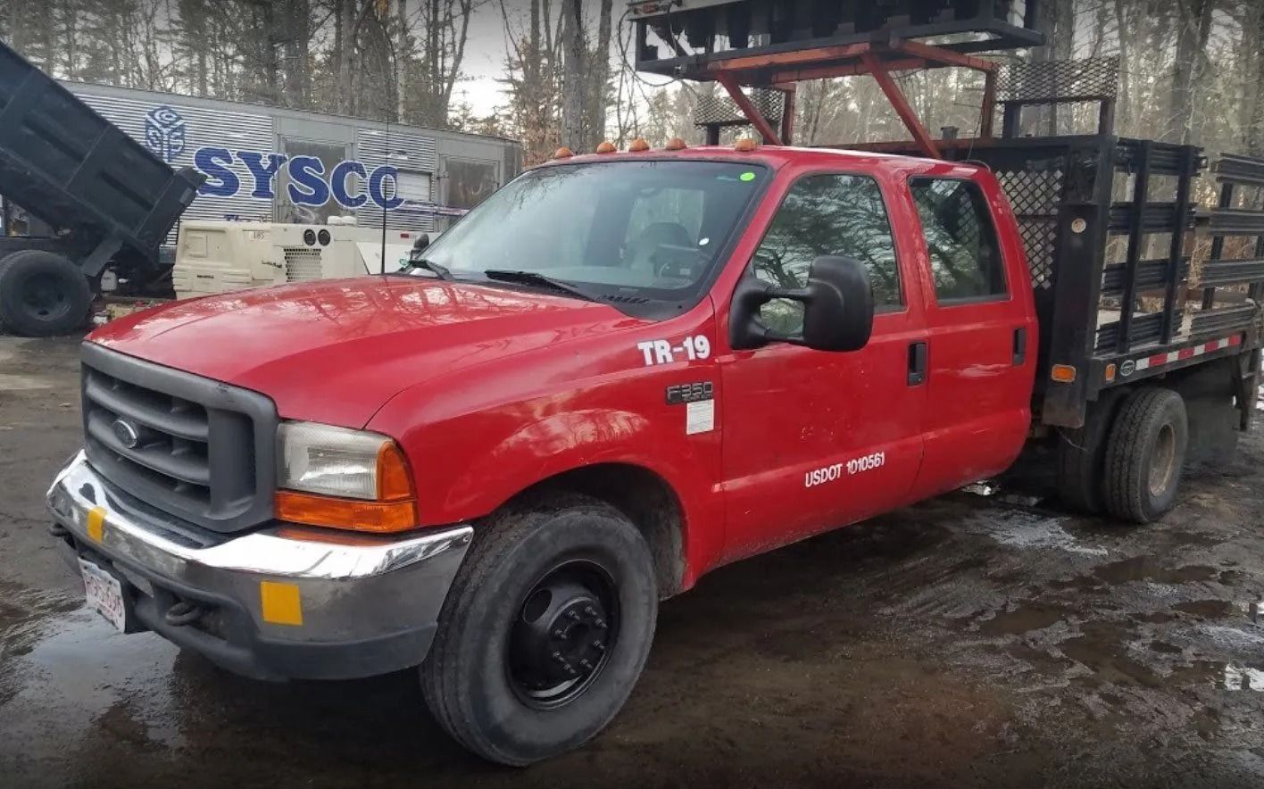 A red Ford F-350 crew cab truck with a flatbed and ladder rack parked in an outdoor lot.